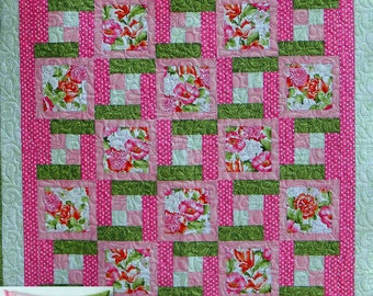 May include: A pink and green quilt with a floral pattern. The quilt is made up of squares and rectangles, and the floral pattern is repeated throughout the quilt. The quilt is bordered in a light green fabric. The quilt is accompanied by a smaller pillow with the same floral pattern.