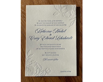May include: A white wedding invitation with blue text announcing the marriage of Katherine Michel to Craig Edward Lehnhardt. The invitation includes the date, time, and location of the wedding ceremony, as well as the dress code: Cocktail Attire.
