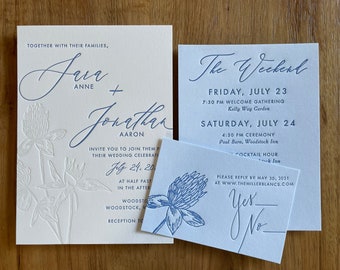 May include: Wedding invitation suite with blue and white lettering. The invitation features a floral design with the names "Sara Anne" and "Jonathan Aaron" and the date "July 24, 20". The RSVP card has the text "Yes" and "No" with a line for guests to check their response.
