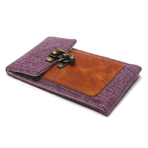 May include: A purple tweed clutch with a brown leather accent and a brass clasp. The rectangular clutch is closed, with the leather patch on the front. The tweed has a herringbone pattern.