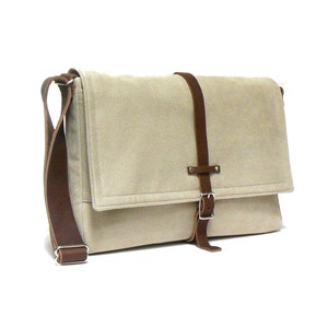 Può includere: Una borsa a tracolla in tela beige con una tracolla in pelle marrone e chiusura a fibbia.