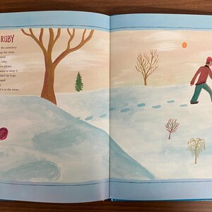 Puede incluir: Un libro abierto con una cubierta azul y una p&aacute;gina blanca que muestra un rub&iacute; rojo en un paisaje nevado. El texto en la p&aacute;gina dice "El Rub&iacute;" y un poema sobre una persona que encuentra un rub&iacute; en la nieve.