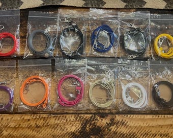 May include: A collection of colorful lanyards in clear plastic bags. The lanyards come in various colors, including red, gray, black, blue, yellow, purple, orange, pink, beige, white, and brown. Each lanyard has a metal clasp.