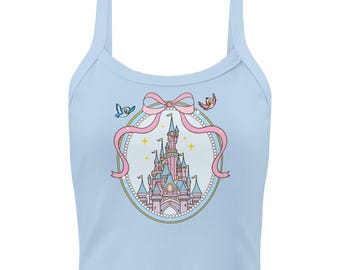 Op de afbeelding: Lichtblauwe tanktop met een roze kasteelafbeelding in een ovaal met parelrand, versierd met een roze strik en twee cartoonvogels. Het kasteel is roze en blauw met gouden accenten. De top heeft dunne bandjes.
