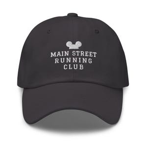 K&ouml;nnte beinhalten: Eine anthrazitfarbene Baseballkappe mit wei&szlig;em Sticktext, der MAIN STREET RUNNING CLUB lautet, platziert unter einem kleinen, wei&szlig; gestickten Symbol in Form einer stilisierten Mauskopf-Silhouette auf der vorderen Kappe.