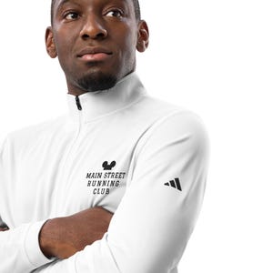 May include: White long-sleeve running shirt with a black Mickey Mouse logo and the text "Main Street Running Club". The shirt has a black Adidas logo on the right sleeve.