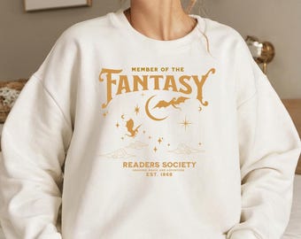 May include: White sweatshirt with a gold graphic that says "Member of the Fantasy Readers Society, Braving Magic and Adventure, Est. 1868". The graphic also includes a crescent moon, stars, and a dragon.