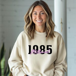 May include: A cream colored sweatshirt with the year 1985 printed in black and the word "Millennial" printed in pink below it.