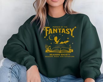 May include: Dark green sweatshirt featuring gold text: "MEMBER OF THE FANTASY READERS SOCIETY, DRAGONS, MAGIC AND ADVENTURE." The design includes a dragon, moon, stars, and an open book. The sweatshirt has a crew neck.
