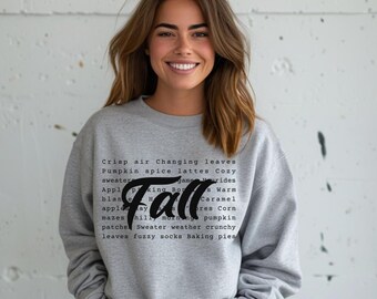 May include: A gray sweatshirt with a black graphic print that says "Fall" and lists fall-themed words like "crisp air", "changing leaves", "pumpkin spice", "lattes", "cozy", "sweater", "baking", "bonfires", "warm", "apple", "hay", "morning", "pumpkin", "patches", "sweater weather", "crunchy leaves", "fuzzy socks", and "baking pies".