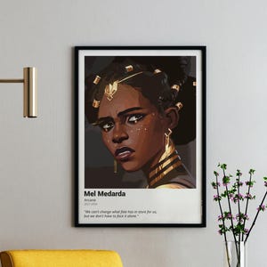 May include: A framed art print featuring Mel Medarda from Arcane. The portrait depicts a woman with dark skin, adorned with gold jewelry. The print includes text: "We can't change what fate has in store for us, but we don't have to face it alone."