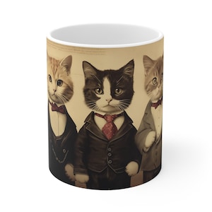 May include: A white ceramic mug with a vintage-style illustration of three cats wearing suits and bow ties. The cats are in a line, with the middle cat being the largest and the other two cats on either side. The background is a light brown color with a faded texture.