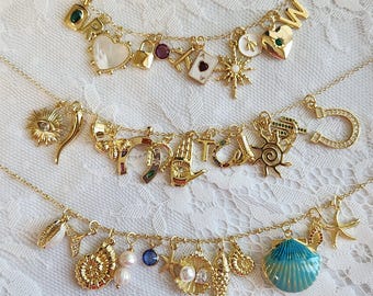 May include: Three gold-tone charm necklaces featuring various pendants. The top necklace has letter charms, a heart, a lock, and a star. The middle necklace includes a sun, horseshoe, and hand. The bottom necklace features seashells, a fish, and a blue shell.