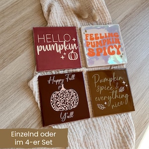 Könnte beinhalten: Vier quadratische Keramikuntersetzer mit herbstlichen Designs. Einer zeigt "Hello Pumpkin", ein anderer "Feeling Pumpkin Spicy". Die anderen beiden zeigen "Happy Fall Y'all" und "Pumpkin spice & everything nice".