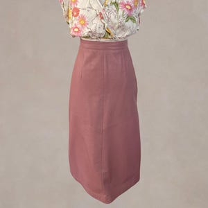 May include: A dusty rose pencil skirt paired with a floral print blouse. The skirt is knee-length and has a tailored fit. The blouse features a V-neck and a pattern of pink and yellow flowers on a cream background. The outfit is displayed on a mannequin.