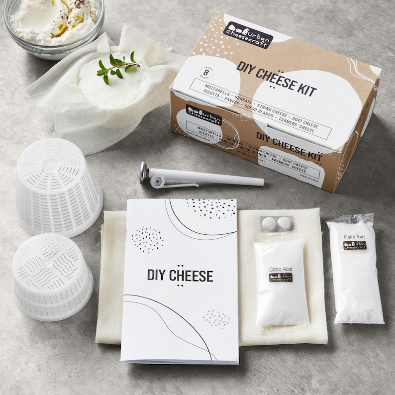 May include: A DIY cheese kit with a cardboard box, ingredients, and tools. The box is labeled "DIY Cheese Kit" and lists cheese types. Included are white cheese molds, a thermometer, and packets of citric acid and flake salt. A booklet reads "DIY CHEESE."