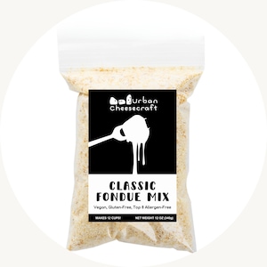 May include: A clear plastic bag filled with a beige powder, labeled "Urban Cheesecraft CLASSIC FONDUE MIX." The black label features a graphic of fondue being poured from a fork. The text indicates it is vegan, gluten-free, and top 8 allergen-free. Net weight is 12 oz (340g).