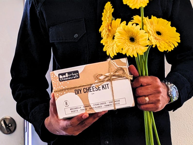 man in nice black shirt arriving with cheese making kit gift and yellow flowers for a date night