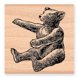 May include: A black and white line drawing of a bear sitting on its haunches with its paws outstretched. The bear is facing to the right and has a simple, cartoon-like style.