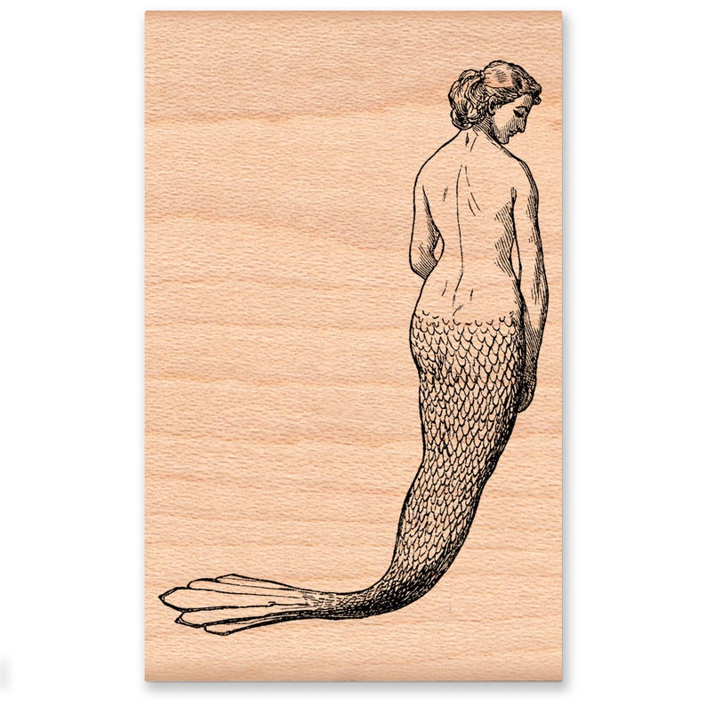 Pu&ograve; includere: Illustrazione in bianco e nero di una sirena su un blocco di legno. La sirena &egrave; raffigurata di spalle, con i capelli raccolti e la coda che si estende verso sinistra. La coda presenta un motivo a scaglie dettagliato.
