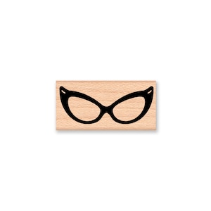 May include: A wooden rubber stamp with a black silhouette of a pair of cat-eye glasses.