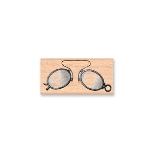 May include: A vintage-style wooden stamp featuring a black and white illustration of a pair of pince-nez glasses.