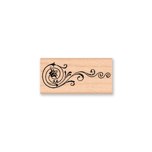 May include: A wooden stamp with a black floral design. The design features a stylized flower with swirling vines.
