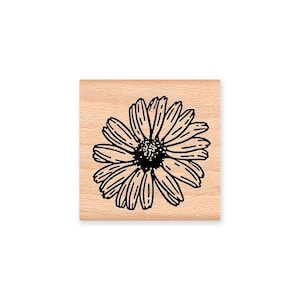 May include: A wooden stamp with a black and white line drawing of a daisy.
