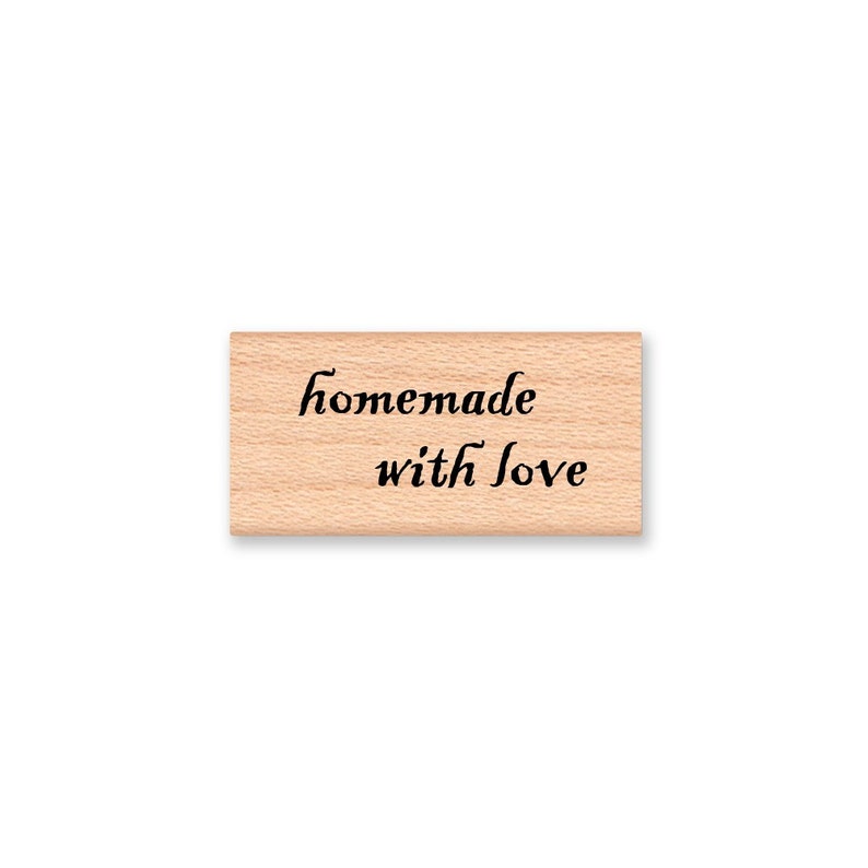 K&ouml;nnte beinhalten: Holzstempel mit dem Text "hausgemacht mit Liebe" in schwarzer Kursivschrift.