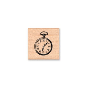 May include: A wooden mounted rubber stamp featuring a black and white illustration of a vintage pocket watch with roman numerals.