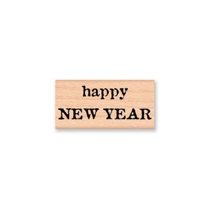 Könnte beinhalten: Ein Holzstempel mit dem Text "happy NEW YEAR" in schwarzer Tinte.