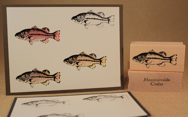 May include: A set of four rubber stamps featuring a black and white illustration of a bass fish. The stamps are mounted on wooden blocks and are labelled "Mountainside Crafts".