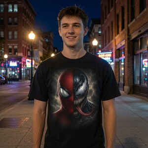 May include: A black short-sleeve t-shirt featuring a graphic print on the chest. The design shows a split face illustration with a red Spider-Man mask on the left side and a black, toothy Venom character with a long red tongue on the right side.