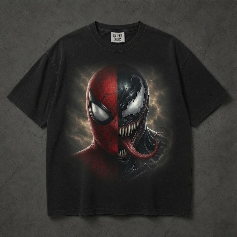 May include: A black short-sleeve t-shirt featuring a split-face graphic print. The left side shows the red and black mask of Spider-Man, while the right side depicts the black, toothy, and long-tongued face of Venom against a dark, cloudy background.