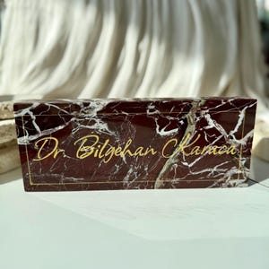 May include: A red marble nameplate with gold lettering that reads "Dr. Bilgehan Karaca".