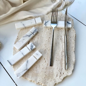 May include: Four white marble rectangular utensil holders with black veining. A silver fork and knife are placed in one of the holders.