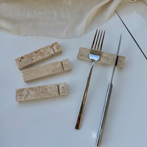 May include: Four beige stone rectangular holders for cutlery, two of which are holding a silver fork and knife.