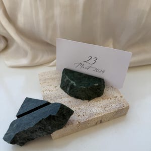May include: A natural stone place card holder with a dark green stone accent. The holder is made of a light beige stone and holds a white card with the date "23 Mart 2024" written on it. The overall theme is rustic and natural.