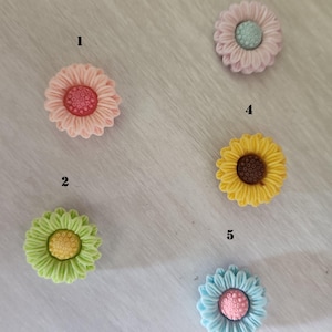 May include: Five colorful, decorative flower-shaped embellishments. The flowers are in shades of pink, green, yellow, and blue, each with a contrasting center. The petals have a textured, layered appearance. These could be used for crafts or embellishing items.
