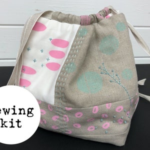 May include: A beige drawstring bag with pink and blue patterned fabric. The bag has a white label that says "sewing kit".