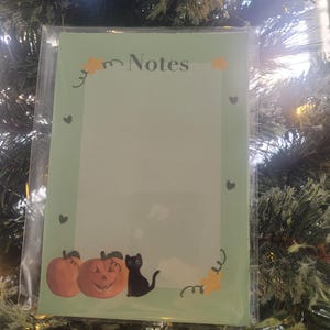 May include: A green notepad with a Halloween theme. The notepad has a black cat, pumpkins, and the word "Notes" at the top.