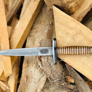 May include: A silver dagger with a wooden handle and a black guard. The blade is sharp and pointed. The handle is made of alternating light and dark wood. The word "CASE" is visible on the blade.