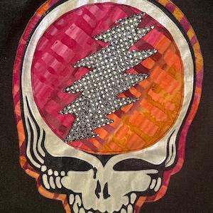 Op de afbeelding: Een kleurrijke patch met een schedelontwerp en een bliksemschicht. De schedel heeft een zilveren omtrek en een zwarte achtergrond. De bliksemschicht is zwart met witte stippen. De achtergrond is een mix van rood, oranje en geel.