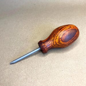 May include: A wooden handled screwdriver with a thin, metal shaft. The handle is made of dark wood with a reddish-brown hue and a swirling grain pattern.