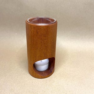 May include: A wooden essential oil diffuser with a glass top and a small tea light candle holder. The diffuser is brown and has a natural wood grain.