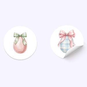 May include: Two round stickers with watercolor Easter egg designs. One sticker features a pink egg with white polka dots and a green bow. The other sticker shows a blue plaid egg with a pink bow and a curled edge.