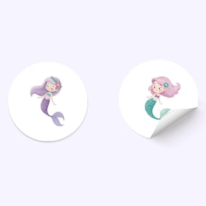 Pu&ograve; includere: Due adesivi rotondi con sirene dei cartoni animati. Una sirena ha capelli e coda viola, l'altra ha capelli rosa e coda turchese. Entrambe le sirene hanno fiori tra i capelli e sorridono.