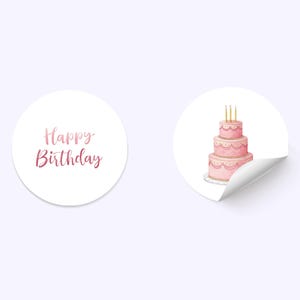 May include: Two white, circular stickers. One displays the text "Happy Birthday" in pink script. The other shows a three-tiered pink cake with gold candles. The cake has decorative icing and sits on a white plate.