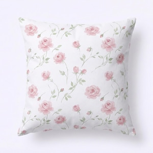 May include: Square white cushion featuring a repeating pattern of pink roses and green stems. The watercolour-style floral design includes full blooms and buds, creating a soft, romantic aesthetic. The cushion is a decorative home accent.