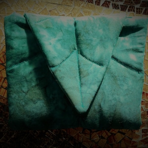 May include: A teal blue quilted fabric pouch with a pointed flap. The pouch is folded in half and has a textured, tie-dye pattern.